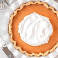 An overhead view of a sweet potato pie topped with homemade whipped cream in a white pie dish.