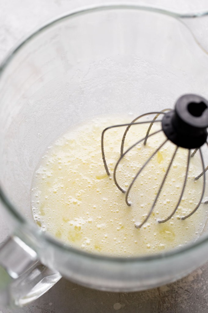 An overhead view of egg whites in a glass mixing bowl with a whisk. 