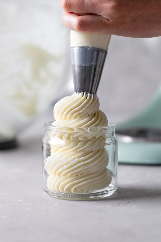 Swiss meringue buttercream being piped into a glass jar from a piping bag. 