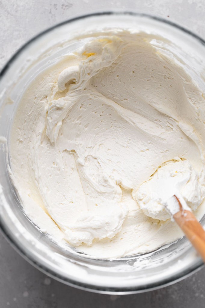 An overhead view of Swiss buttercream in a mixing bowl with a rubber spatula. 