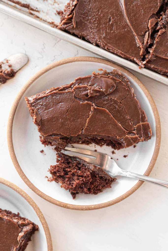 An overhead view of a slice of Texas sheet cake on a white plate. A bite has been cut off. 