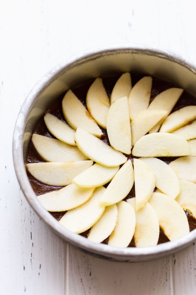 A round metal baking dish holding the caramel topping and apples arranged into a circle.