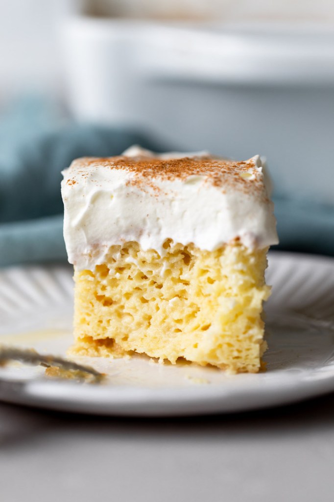 Side view of a slice of tres leches cake on a white plate. A blue towel rests in the background.