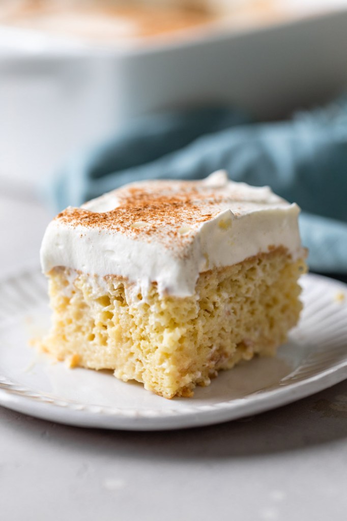 A slice of the best tres leches cake on a white plate. A blue towel rests in the background.