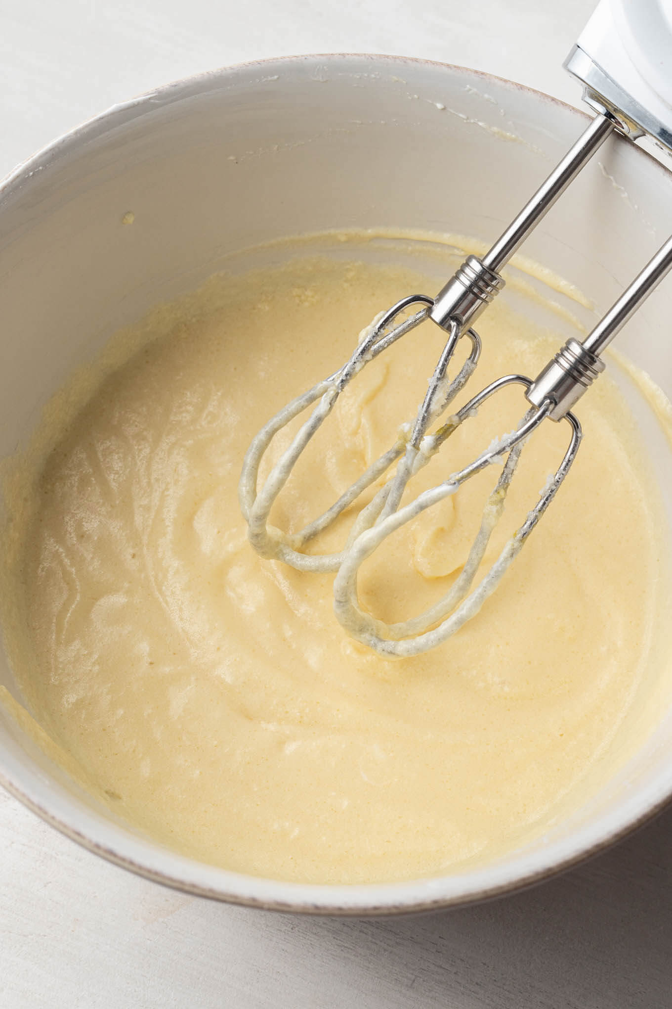 Wet ingredients for cupcakes in a mixing bowl with a handheld mixer.