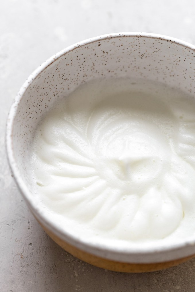 Egg whites beat to stiff peaks in a speckled mixing bowl.