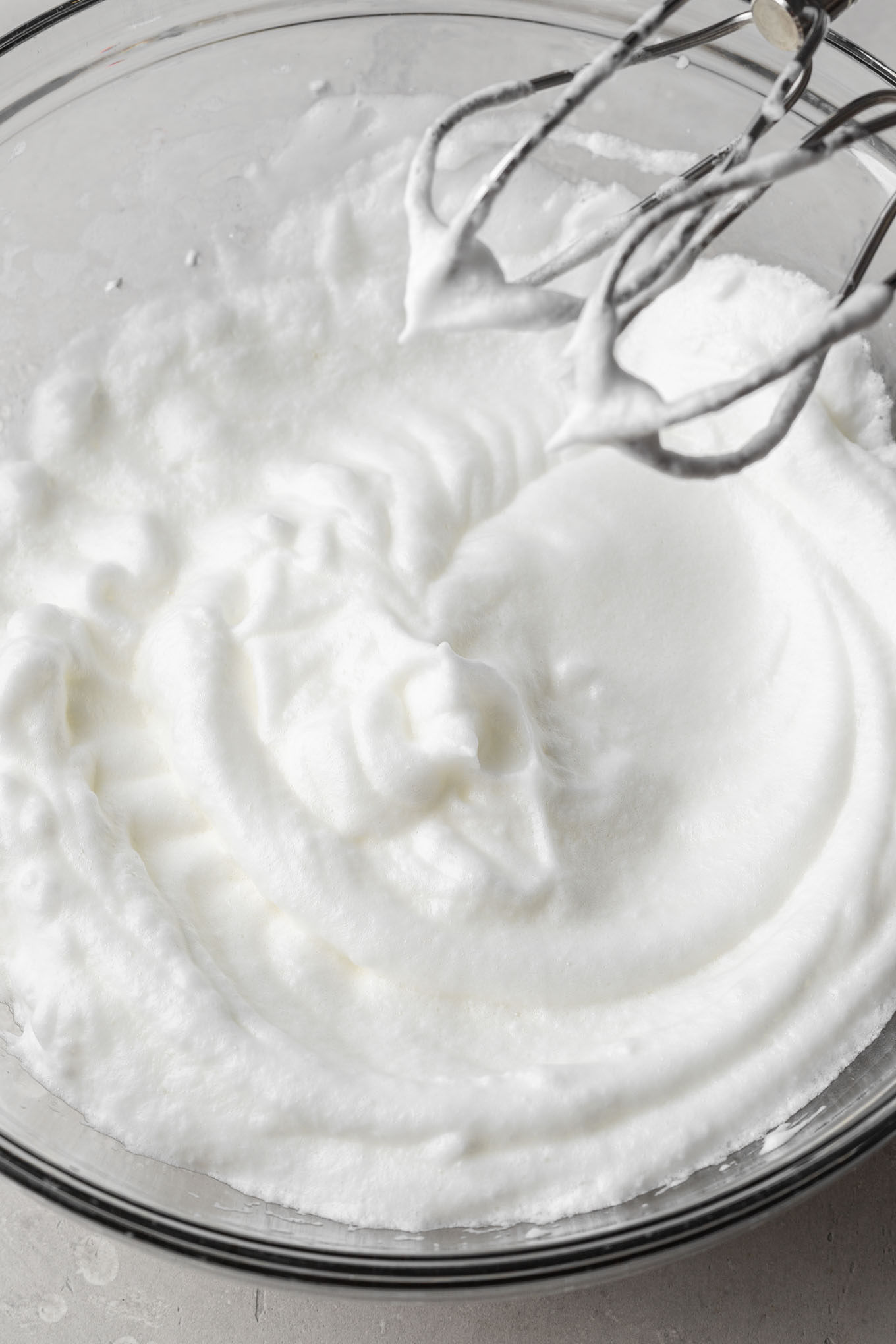 Stiff egg whites in a glass mixing bowl.