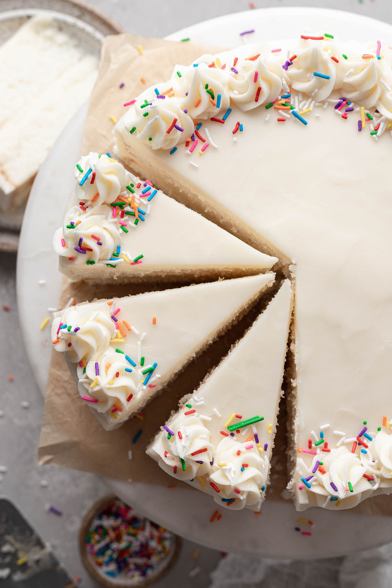 An overhead view of a homemade white cake on a cake stand. Three slices have been cut. 