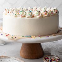 A white cake topped with sprinkles on a marble cake stand.