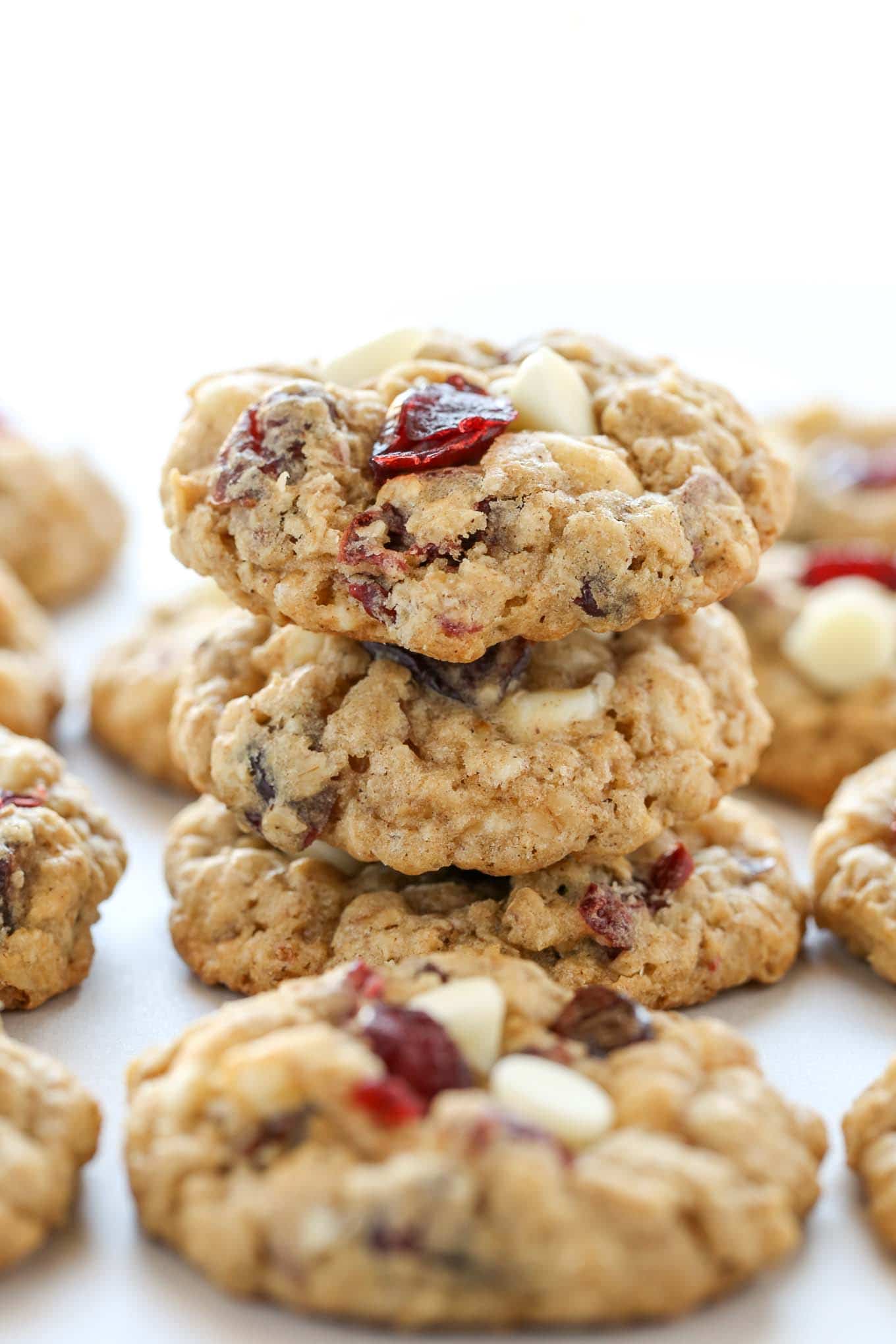 A stack of three white chocolate cranberry oatmeal cookies. Additional cookies surround the stack. 