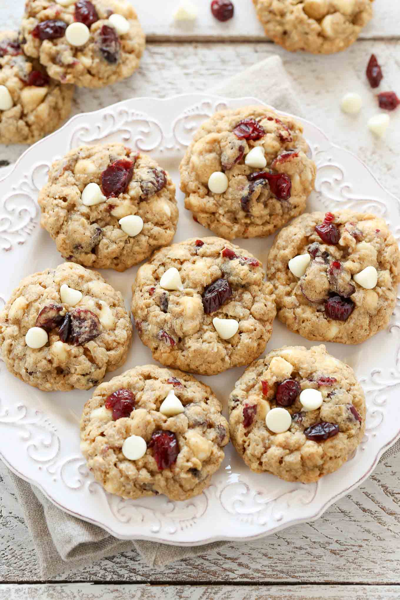 Overhead view of seven oatmeal cranberry cookies on a white plate. Additional cookies rest on the counter. 