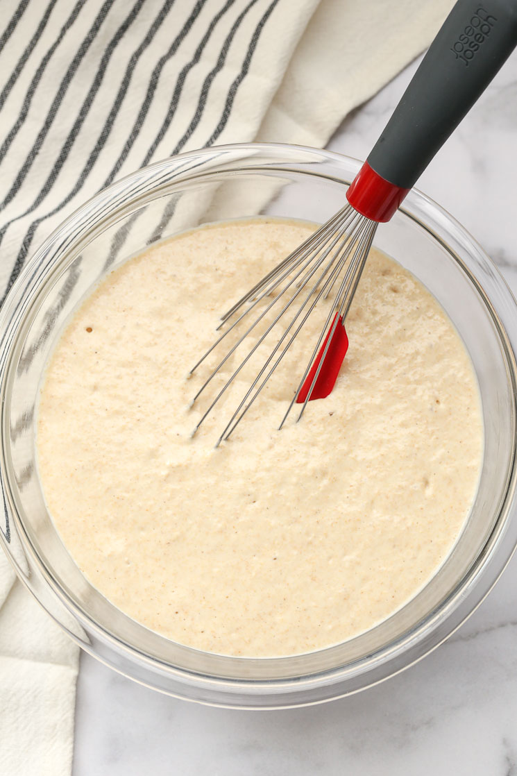 A clear bowl with pancake batter and a whisk.