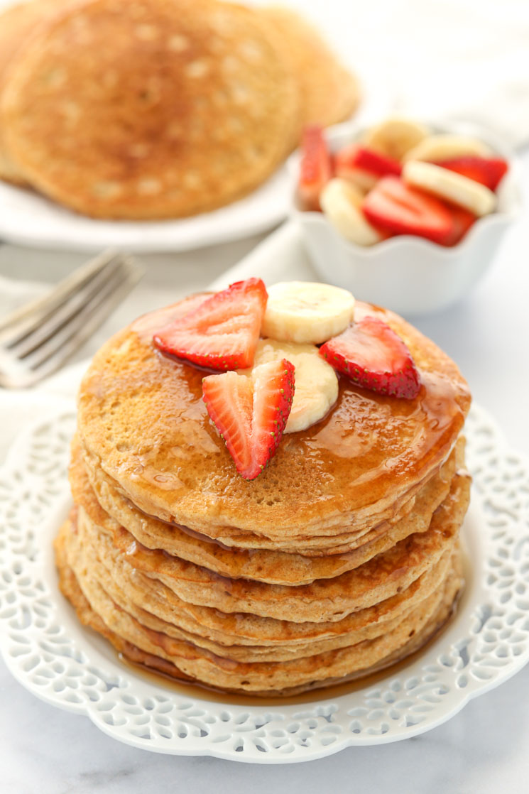 A stack of whole wheat pancakes topped with strawberry slices, banana slices, and maple syrup.