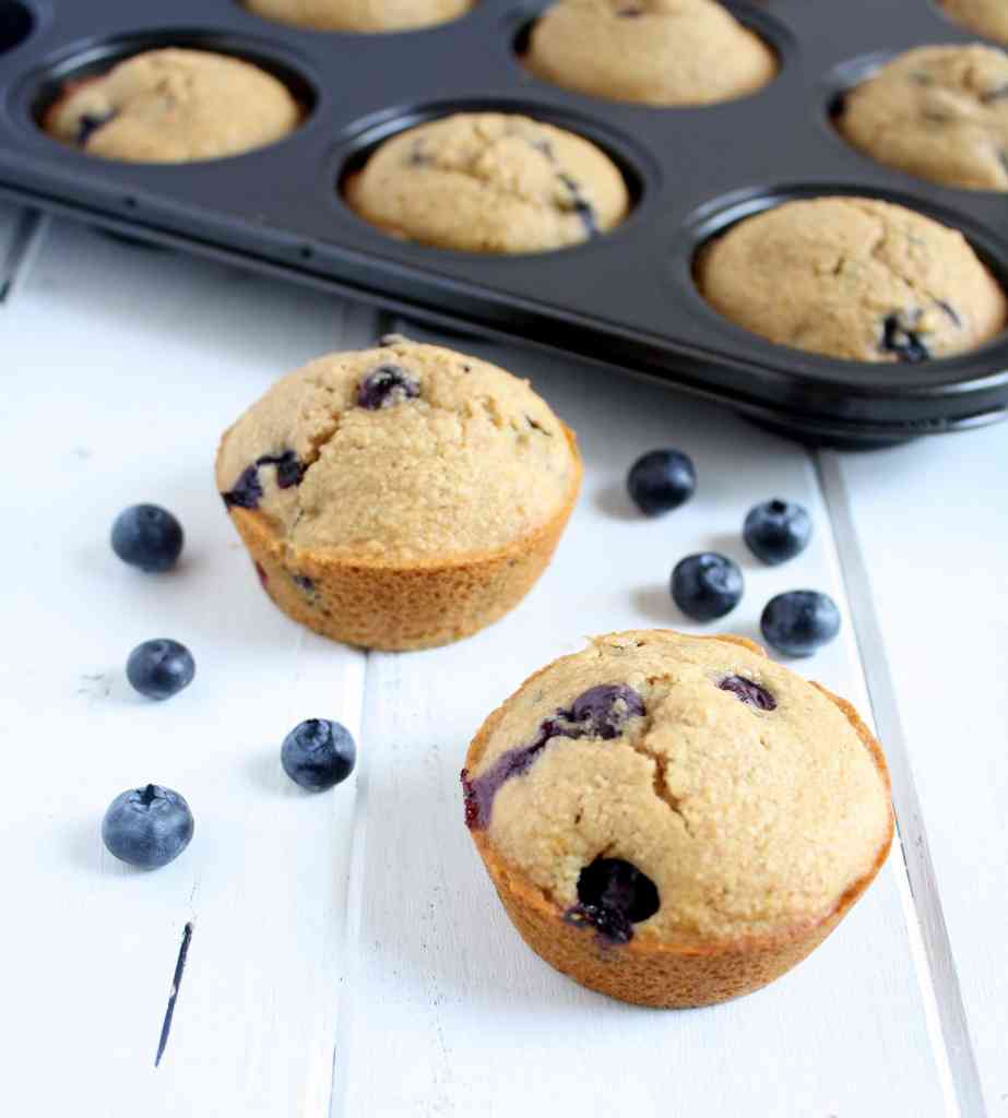 Two Whole Wheat Blueberry Muffins sitting in front of a pan of muffins. 