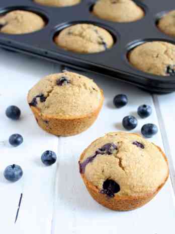 Two Whole Wheat Blueberry Muffins sitting in front of a pan of muffins.