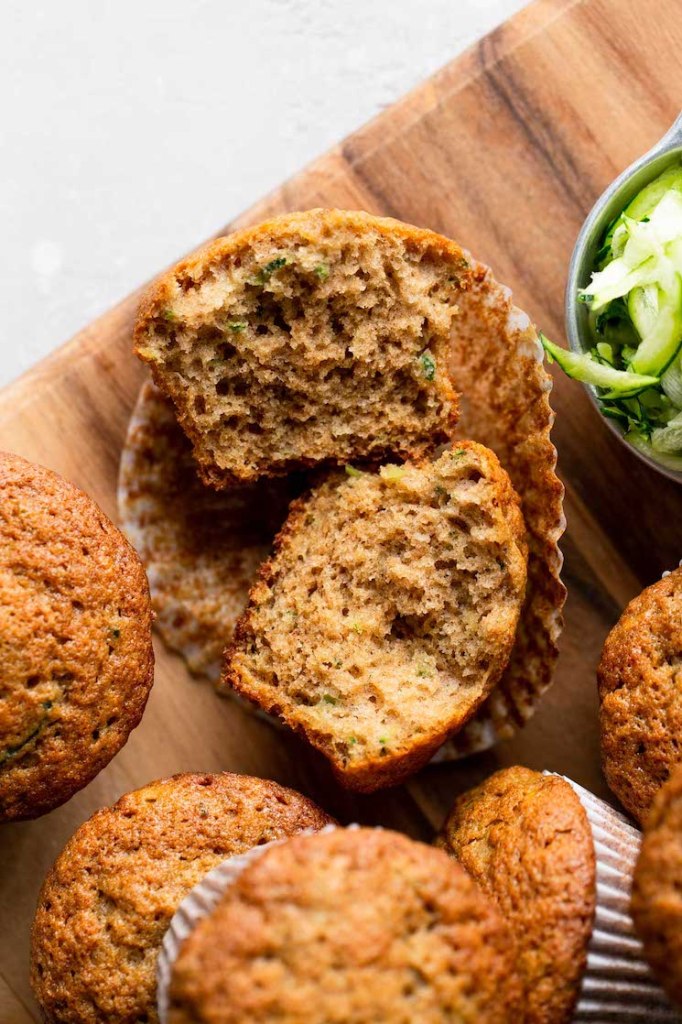 An overhead view of zucchini muffins on a wood cutting board. One muffin has been cut in half and others are lying on their sides. 